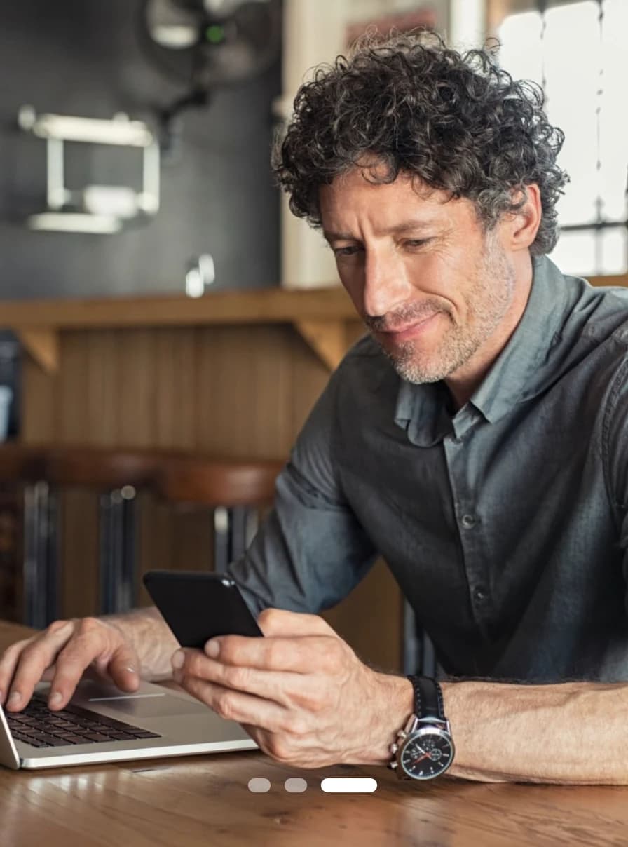 A practitioner checking a drtalk reply on a phone beside a laptop at a cafe